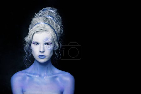 Téléchargez les photos : Maquillage fantastique. Belle femme modèle avec peau blanche et bleue et coiffure créative sur fond noir - en image libre de droit