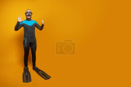 Scuba diver man showing six fingers up on yellow studio wall background