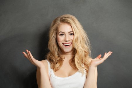 Wunderschöne gesunde überraschte Frau Modemodel mit niedlichem Lächeln hält leere Handfläche Hand vor schwarzem Studiowand Hintergrund