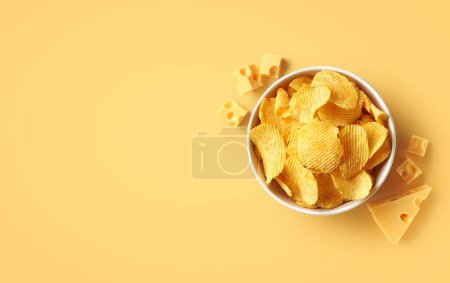 Photo for Bowl of crispy potato chips or crisps with cheese flavor on light yellow background, top view, empty space for text - Royalty Free Image