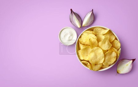 Foto de Cuenco de papas fritas crujientes o patatas fritas con sabor a crema agria y cebolla sobre fondo púrpura claro, vista superior, espacio vacío para texto - Imagen libre de derechos