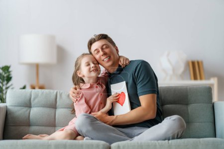 Photo for Child daughter is congratulating her father and giving him postcard. Dad and girl are smiling and hugging. Family holiday and togetherness. - Royalty Free Image