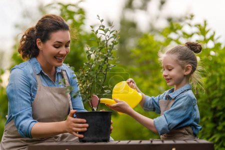 Téléchargez les photos : Joyeux jardinage mère et fille dans la cour. Enfant aider sa mère et apprendre la botanique. - en image libre de droit