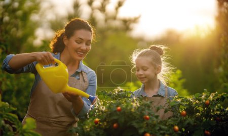 Téléchargez les photos : Joyeux jardinage mère et fille dans la cour. Enfant aider sa mère et apprendre la botanique. - en image libre de droit