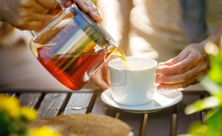 Téléchargez les photos : Verser le thé noir dans une tasse en verre sur une table en bois le matin ensoleillé. - en image libre de droit