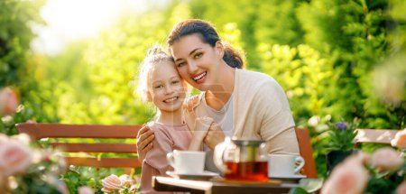 Photo for Happy little girl and her mother drinking tea in summer morning. Family sitting in the garden with cups and enjoying the conversation. - Royalty Free Image