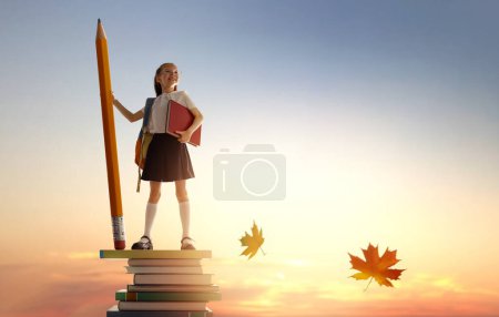 Photo for Back to school! Happy cute industrious child standing on the tower of books and holding a huge pencil on background of sunset sky. Concept of education and reading. The development of the imagination. - Royalty Free Image