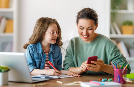 Foto de Niño feliz y adulto están sentados en el escritorio. Chica haciendo deberes o educación en línea. - Imagen libre de derechos