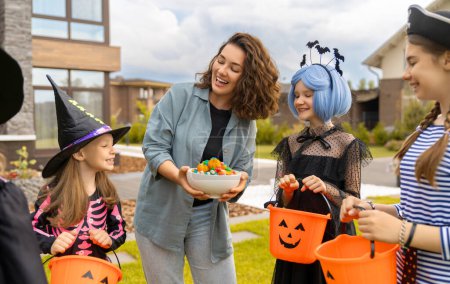 Photo for Happy people celebrating Halloween. Adult is treating with sweets children outdoors. - Royalty Free Image
