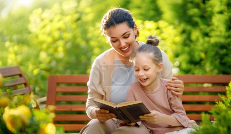 Foto de Feliz niña y su madre leyendo un libro en la mañana de verano. Familia sentada en el jardín y disfrutando juntos. - Imagen libre de derechos
