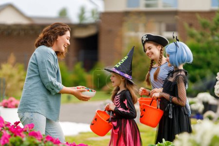 Photo for Happy people celebrating Halloween. Adult is treating with sweets children outdoors. - Royalty Free Image