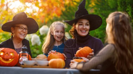 Téléchargez les photos : Bonne famille se préparant pour Halloween. Mère, grand-mère et enfants sculptant des citrouilles dans la cour arrière de la maison. - en image libre de droit