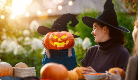 Téléchargez les photos : Bonne famille se préparant pour Halloween. Mère et enfants sculptant des citrouilles dans la cour de la maison. - en image libre de droit