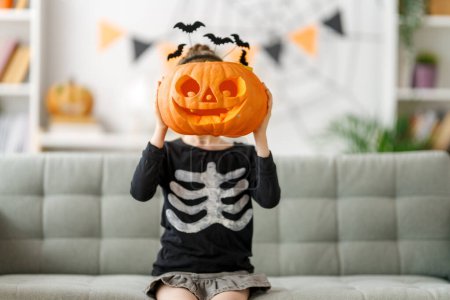 Foto de Lindo niño pequeño con calabaza tallada. Chica feliz preparándose para Halloween. Chico gracioso en casa. - Imagen libre de derechos