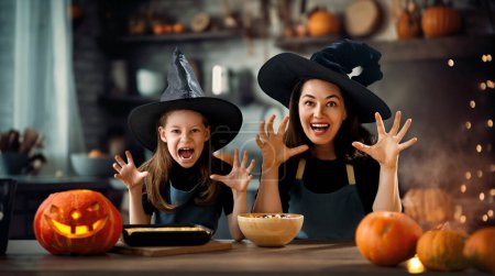 Téléchargez les photos : Mère et sa fille s'amusent à la maison. Happy Family se prépare pour Halloween. Maman et enfant cuisinent des plats de fête dans la cuisine
. - en image libre de droit
