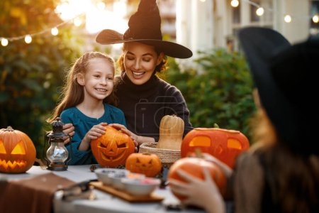 Téléchargez les photos : Bonne famille se préparant pour Halloween. Mère et enfants sculptant des citrouilles dans la cour de la maison. - en image libre de droit