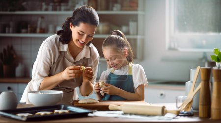 Téléchargez les photos : Une famille heureuse et aimante prépare la boulangerie ensemble. Mère et fille enfant fille cuisinent des biscuits et s'amusent dans la cuisine. Nourriture maison et petite aide. - en image libre de droit