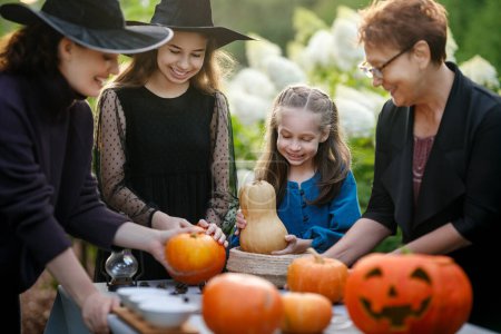 Foto de Familia feliz preparándose para Halloween. Madre, abuela y niños tallando calabazas en el patio trasero de la casa. - Imagen libre de derechos