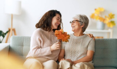 Photo for Happy adult woman and her senior mother with autumn leaves indoors. - Royalty Free Image