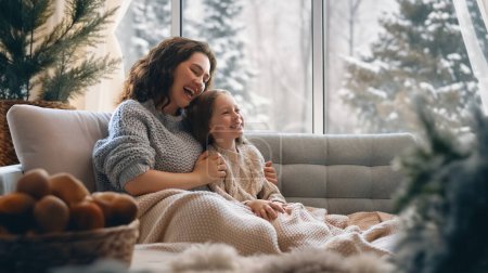 Photo for Happy loving family. Mother and daughter are hugging and enjoying winter nature in the  window. - Royalty Free Image