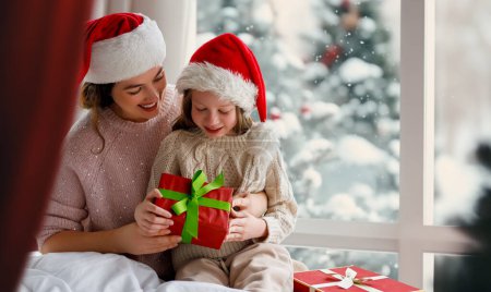 Téléchargez les photos : Joyeux Noël et Joyeuses Fêtes. Joyeux maman et sa fille mignonne fille échanger des cadeaux. Parent et petit enfant s'amusent près de l'arbre à l'intérieur. Matin Noël. - en image libre de droit