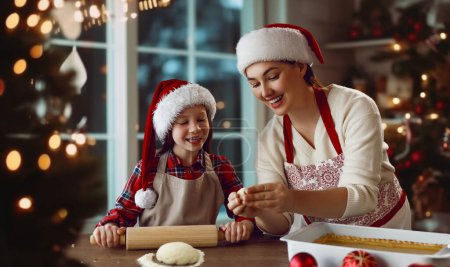 Foto de Feliz Navidad y Felices Fiestas. Preparación familiar comida de vacaciones. Madre e hija cocinando pastel. - Imagen libre de derechos
