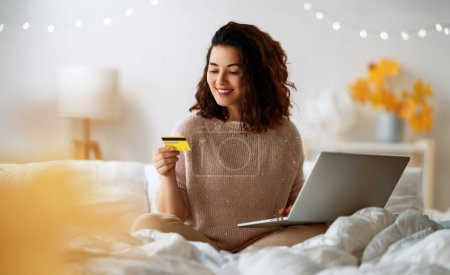 Foto de Mujer está haciendo compras en línea. Chica está haciendo compras usando el ordenador portátil y tarjeta de crédito en casa. - Imagen libre de derechos