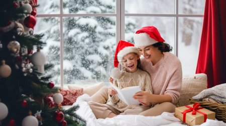 Photo for Merry Christmas and Happy Holidays. Cheerful mom and her cute daughter girl reading a book. Parent and little child having fun near tree indoors. Morning Xmas. - Royalty Free Image