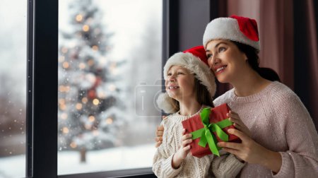 Téléchargez les photos : Joyeux Noël et Joyeuses Fêtes. Joyeux maman et sa fille mignonne fille échanger des cadeaux. Parent et petit enfant s'amusent près de l'arbre à l'intérieur. Matin Noël. - en image libre de droit