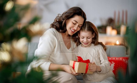 Photo for Merry Christmas and Happy Holidays. Cheerful mom and her cute daughter girl exchanging gifts. Parent and little child having fun near tree indoors. - Royalty Free Image