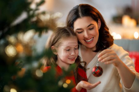Foto de Feliz Navidad, Felices Fiestas. Mamá e hija cerca del árbol en el interior. La mañana antes de Navidad. - Imagen libre de derechos