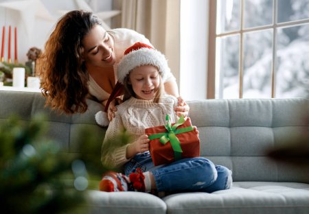 Téléchargez les photos : Joyeux Noël et Joyeuses Fêtes. Joyeux maman et sa fille mignonne fille échanger des cadeaux. Parent et petit enfant s'amusent près d'un arbre à l'intérieur. - en image libre de droit