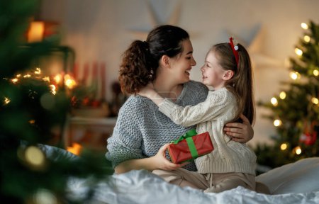 Photo for Merry Christmas and Happy Holidays. Cheerful mom and her cute daughter girl exchanging gifts. Parent and little child having fun near tree indoors. Loving family with presents in room. - Royalty Free Image