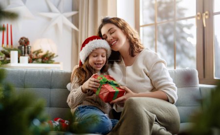 Téléchargez les photos : Joyeux Noël et Joyeuses Fêtes. Joyeux maman et sa fille mignonne fille échanger des cadeaux. Parent et petit enfant s'amusent près d'un arbre à l'intérieur. - en image libre de droit