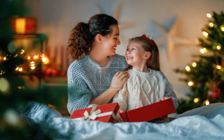 Téléchargez les photos : Joyeux Noël et Joyeuses Fêtes. Joyeux maman et sa fille mignonne fille échanger des cadeaux. Parent et petit enfant s'amusent près de l'arbre à l'intérieur. Famille aimante avec des cadeaux dans la chambre. - en image libre de droit