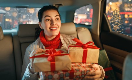 Téléchargez les photos : Femme tient des cadeaux et les livre en voiture à la maison. Concept de vacances. Temps de la veille de Noël. - en image libre de droit