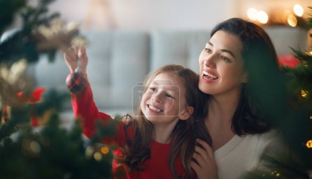 Téléchargez les photos : Joyeux Noël, Joyeuses Fêtes. Maman et fille près de l'arbre à l'intérieur. Le matin avant Noël. - en image libre de droit