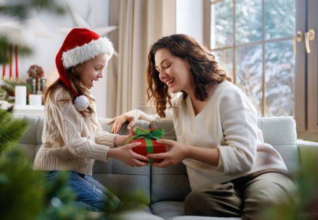 Photo for Merry Christmas and Happy Holidays. Cheerful mom and her cute daughter girl exchanging gifts. Parent and little child having fun near tree indoors. - Royalty Free Image