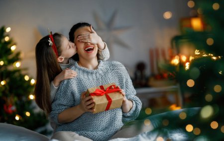 Téléchargez les photos : Joyeux Noël et Joyeuses Fêtes. Joyeux maman et sa fille mignonne fille échanger des cadeaux. Parent et petit enfant s'amusent près de l'arbre à l'intérieur. Famille aimante avec des cadeaux dans la chambre. - en image libre de droit