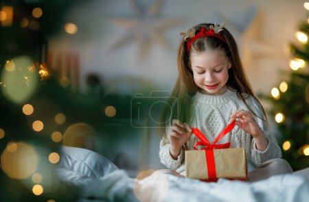 Téléchargez les photos : Joyeux Noël et Joyeuses Fêtes. Joyeux enfant fille mignonne avec un cadeau. Le gamin s'amuse près de l'arbre. - en image libre de droit
