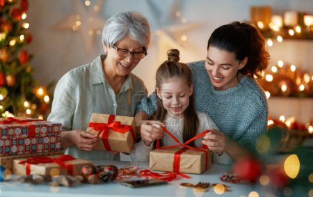 Photo for Happy Holidays. Cheerful grandmother, mother and cute daughter girl preparing for Christmas. People wrapping gifts, decorating home. Loving family with presents in room. - Royalty Free Image
