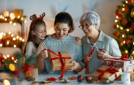Photo for Happy Holidays. Cheerful grandmother, mother and cute daughter girl preparing for Christmas. People wrapping gifts, decorating home. Loving family with presents in room. - Royalty Free Image