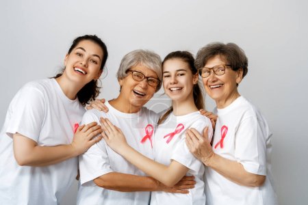 Téléchargez les photos : Des femmes souriantes avec un ruban de satin rose symbolisant le concept de sensibilisation à la maladie, exprimant solidarité et soutien aux patients atteints de cancer et aux survivants. Différentes générations de personnes - en image libre de droit