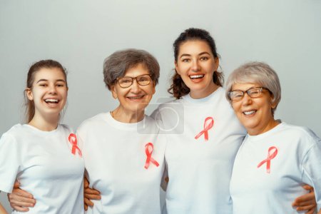 Foto de Las mujeres sonrientes con cinta de satén rosa simbolizan el concepto de conciencia de la enfermedad, expresando solidaridad y apoyo a los pacientes y sobrevivientes de cáncer. Diferentes generaciones de personas - Imagen libre de derechos