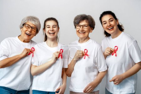 Photo for Smiling women with pink satin ribbon symbolizing concept of illness awareness, expressing solidarity and support for cancer patients and survivors. Different generations of people - Royalty Free Image