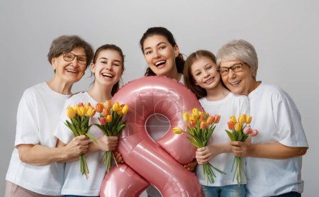 Téléchargez les photos : Joyeuse journée des femmes ! Les filles des enfants félicitent maman et les grands-mères de leur donner des fleurs tulipes. Grannys, maman et les filles souriant sur fond gris clair. Vacances en famille et convivialité. - en image libre de droit