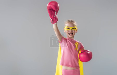 Photo for Child in boxing gloves with a yellow ribbon as a symbol of the fight against cancer. Increasing the level of knowledge about kids who have overcome tumor diseases. - Royalty Free Image