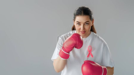 Foto de Mujer en guantes de boxeo con una cinta rosa como símbolo de la lucha contra el cáncer. Aumentar el nivel de conocimiento sobre las personas que han superado las enfermedades tumorales. - Imagen libre de derechos