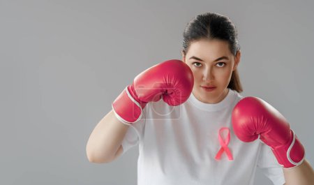 Foto de Mujer en guantes de boxeo con una cinta rosa como símbolo de la lucha contra el cáncer. Aumentar el nivel de conocimiento sobre las personas que han superado las enfermedades tumorales. - Imagen libre de derechos