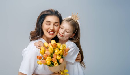 Téléchargez les photos : Joyeuse journée des femmes. L'enfant félicite maman et lui donne des fleurs jaunes. Maman et fille souriant sur fond gris clair. Vacances en famille et convivialité. - en image libre de droit